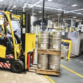 Worker using forklift for steel kegs in warehouse